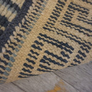 Textured dark blue and tan rug with a geometric pattern is curled over gray distressed wood.