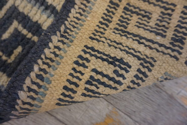 Textured dark blue and tan rug with a geometric pattern is curled over gray distressed wood.