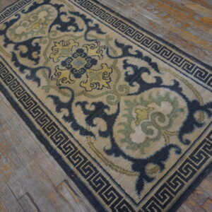 Navy, tan, and green runner rug featuring a detailed scroll pattern and Greek key border on distressed wood planks.