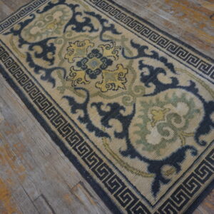 Beige runner with dark blue Greek key border and scrolling motifs in yellow and sage green on wood flooring.