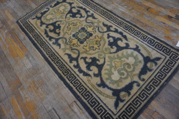 Beige runner with dark blue greek key border and scrolling motifs in yellow and sage green on wood flooring.