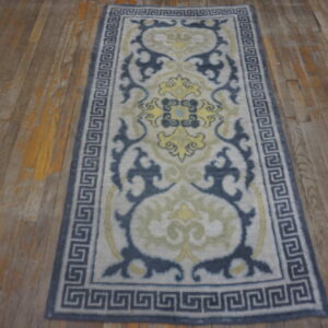 Low-pile runner in gray, navy, and yellow with an elaborate border on distressed wood flooring.
