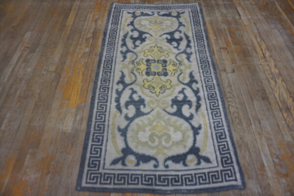 Low-pile runner in gray, navy, and yellow with an elaborate border on distressed wood flooring.