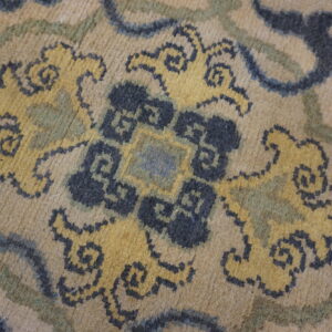 Low-pile rug detail showing beige, dark blue, and yellow stylized floral and scrolling patterns.