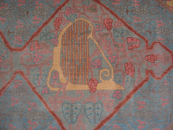 A muted gray-blue rug features a central diamond medallion with a stylized gold harp and pink floral patterns.