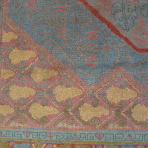 Close view of a blue and pink traditional patterned rug with gold accents and geometric borders.