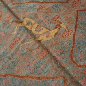 Muted grey-blue rug with rust borders, pink motifs, and a central yellow deer design.