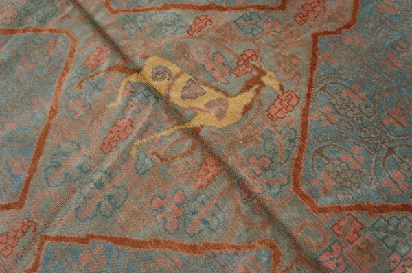 Muted grey-blue rug with rust borders, pink motifs, and a central yellow deer design.