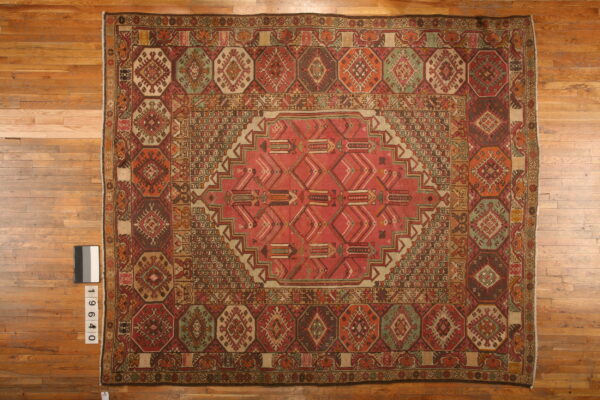 Geometric red, brown, and green patterned low-pile rug displayed flat on light-toned hardwood flooring.
