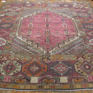 Rectangular geometric rug in pink, burgundy, orange, and sage green laid on bright hardwood flooring.