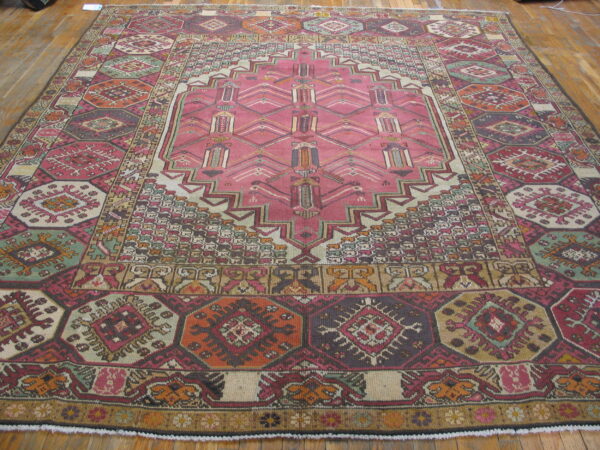 Rectangular geometric rug in pink, burgundy, orange, and sage green laid on bright hardwood flooring.