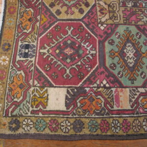 Geometric rug detail showing panels of red, teal, and gold patterns next to rustic wood floor.