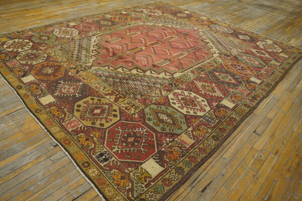 Low-pile rug with a complex, multicolored geometric design, including coral, red, and green, on distressed wood planks.