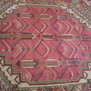 Rose pink rug with complex geometric patterns inside a stepped medallion and multicolored tribal borders.