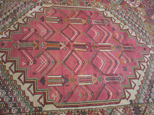 Rose pink rug with complex geometric patterns inside a stepped medallion and multicolored tribal borders.