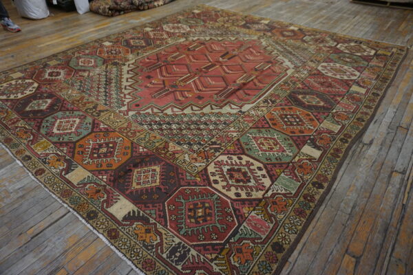 Low-pile geometric rug with complex red, green, orange, and brown patterns rests on worn wood planks.