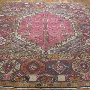 Geometric rug with a large pink central medallion and borders of rust, sage, and burgundy on wood flooring.