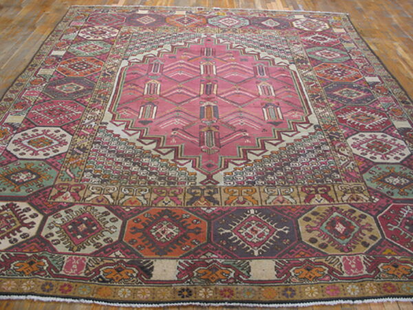 Geometric rug with a large pink central medallion and borders of rust, sage, and burgundy on wood flooring.