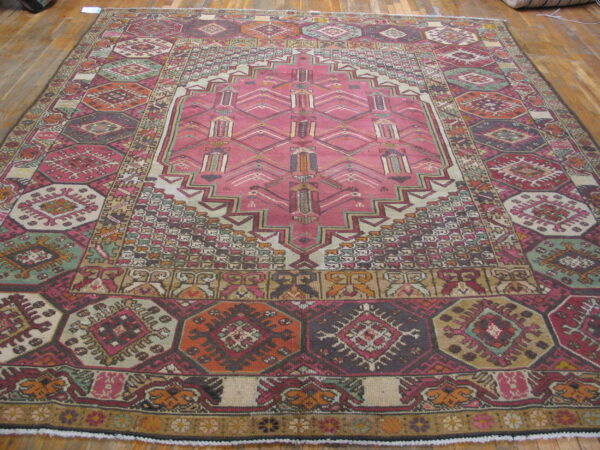 Rose pink and multicolor geometric rug with complex borders lying on wooden plank flooring.