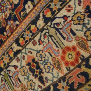 Closeup of a traditional rug border and field intersection with navy, cream, red, and gold motifs.