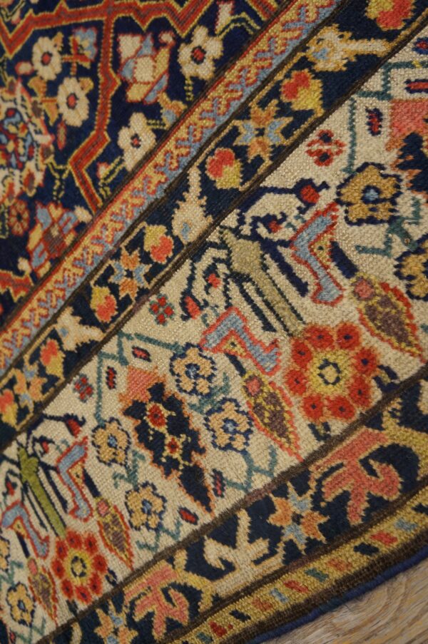 Closeup of a traditional rug border and field intersection with navy, cream, red, and gold motifs.