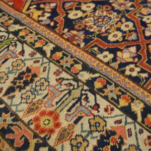 Close-up of a low-pile traditional rug with navy field and intricate cream, red, and gold floral borders.