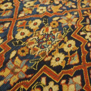 Detail of a woven rug showing a dense floral pattern and stepped lattice in navy, gold, and rust.