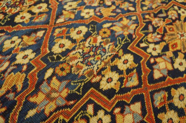 Detail of a woven rug showing a dense floral pattern and stepped lattice in navy, gold, and rust.