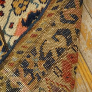 Low-pile rug with floral motifs rolled back to show the woven foundation on peeling wood planks.