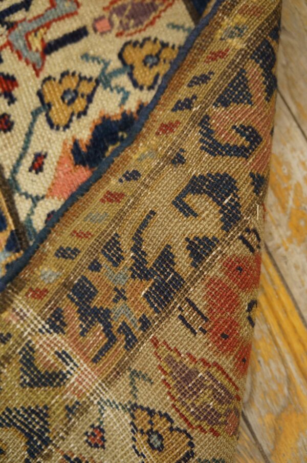 Low-pile rug with floral motifs rolled back to show the woven foundation on peeling wood planks.