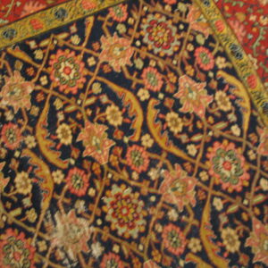 Intricate close-up of a low pile rug with a dark blue field and salmon, gold, and red floral motifs.