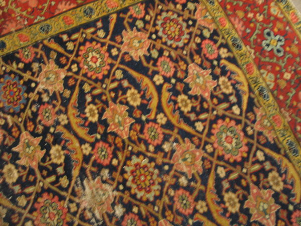 Intricate close-up of a low pile rug with a dark blue field and salmon, gold, and red floral motifs.