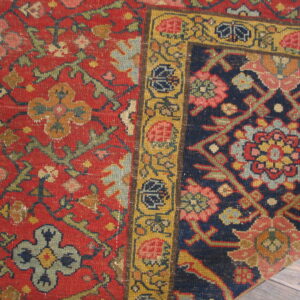 Close view of a richly patterned rug displaying red, navy blue, and yellow floral motifs on wood floor.