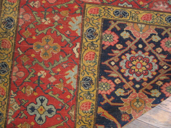 Close view of a richly patterned rug displaying red, navy blue, and yellow floral motifs on wood floor.