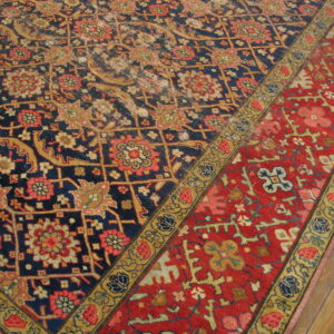 Close-up of a low-pile rug with navy, red, and gold intricate floral designs on wood planks.