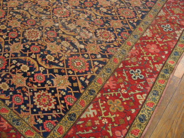Close-up of a low-pile rug with navy, red, and gold intricate floral designs on wood planks.