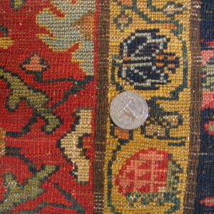 Close-up of a low-pile knotted rug showing red, gold, and navy geometric patterns next to a quarter coin.