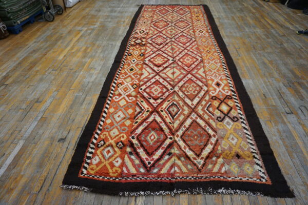 Textured runner rug with multicolored geometric diamond designs in orange, red, and yellow on distressed wood planks.