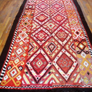 Shaggy runner rug with vibrant red, yellow, and black geometric designs, framed by solid dark brown borders.