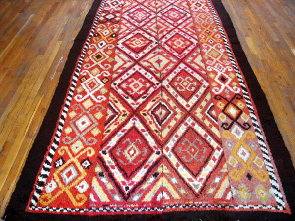 Shaggy runner rug with vibrant red, yellow, and black geometric designs, framed by solid dark brown borders.