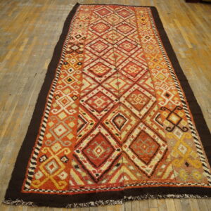 High-pile runner rug featuring orange, red, and yellow diamond motifs and a dark brown border on wood flooring.