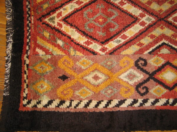 High-pile rug with geometric patterns in red, gold, and dark brown, lying on a wooden floor.