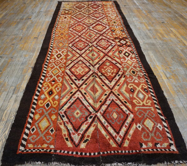 Long, textured rug featuring red and yellow diamonds with dark brown shaggy borders on worn wood floors.