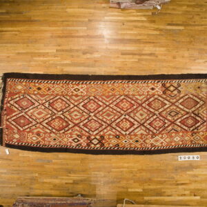 Rectangular rug with red, gold, and cream diamond patterns and a dark brown border on light wood flooring.