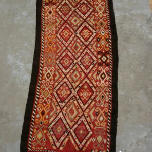 Runner rug displaying a bright red and gold repeating diamond pattern with dark brown outer edges on concrete.