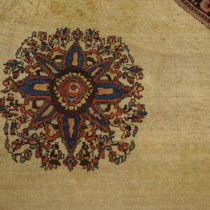Low-pile tan rug with a colorful blue and red central floral motif adjacent to a dark, stepped border.