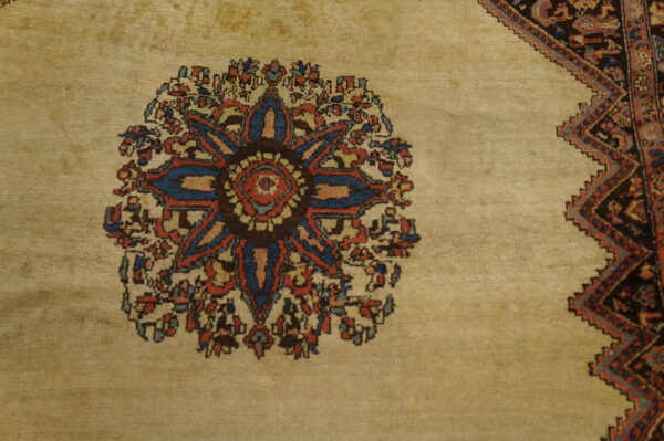 Low-pile tan rug with a colorful blue and red central floral motif adjacent to a dark, stepped border.
