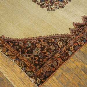 Diagonal view of a low-pile beige rug with complex dark brown and terracotta borders on distressed wood planks.