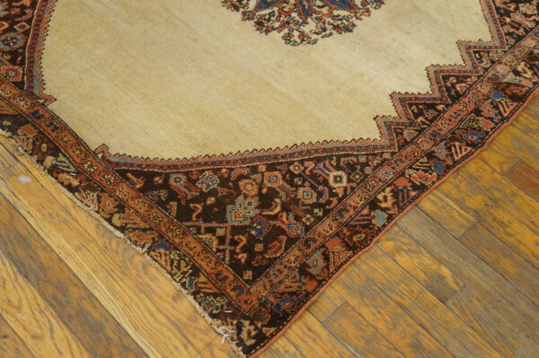 Diagonal view of a low-pile beige rug with complex dark brown and terracotta borders on distressed wood planks.