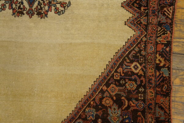 Beige rug field transitions to a dark, stepped border with red and blue geometric patterns over wood floor.